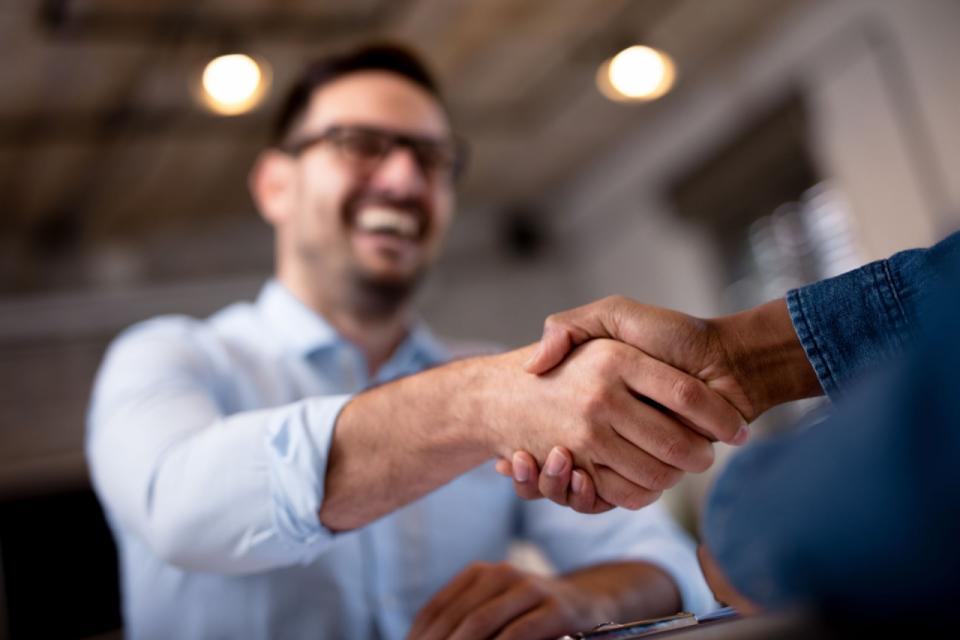 Two business people shake hands and smile.