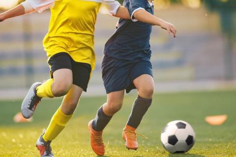 Two boys play football on an outdoor pitch