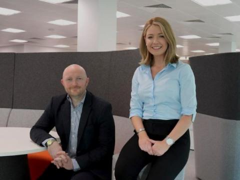 Two people in a bright office smile at the camera.