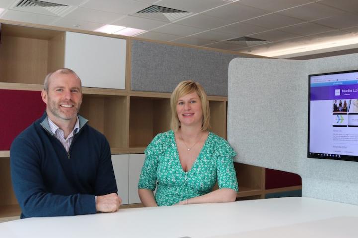 Two people smile at the camera in a bright office