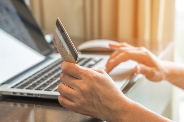 A person sits at the computer holding their credit card