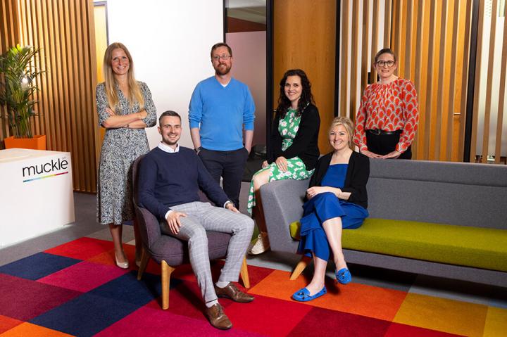 six lawyers, two sitting on chairs and four standing behind them