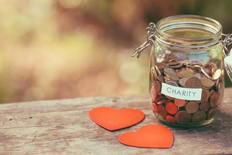 Pennies in a glass jar with a label that says 'charity' on top of a wooden table with heart-shaped Post-It notes next to it.
