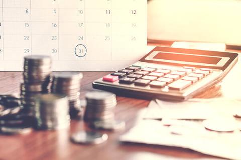 Close up of coins and a calculator on a table in front of a calendar