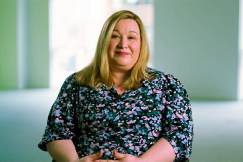 Sam Pritchard sitting on a chair, wearing a patterned dress, looking at the camera