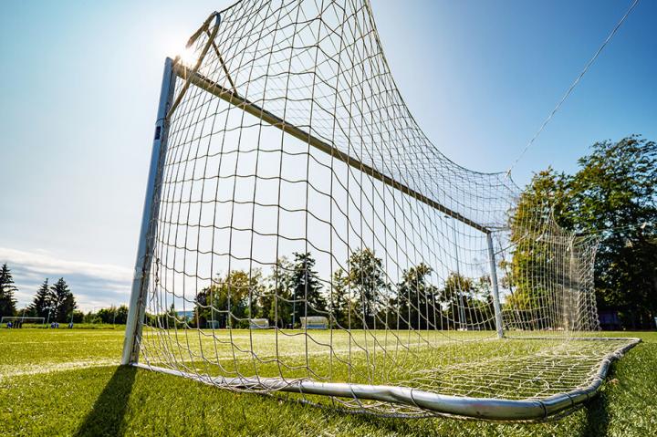 Photo behind a football goal post, looking out onto the pitch with a blue sky