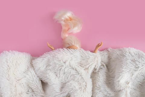a doll head and hair sticking out from under a fur blanket on a pink background
