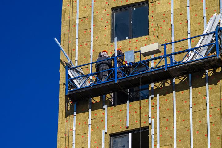 workmen high up on a building installing cladding