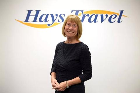 Dame Irene Hays in front of a white wall with the Hays Travel logo