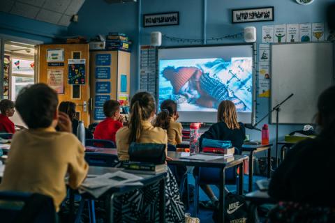 school children sitting at desks and looking at a projector screen