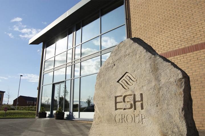 A stone slab with Esh Group's logo in front of Esh Group's office building