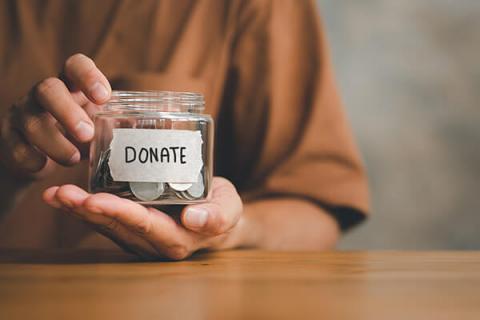 A close up of hands holding a jar with 'donate' written on with coins in the jar