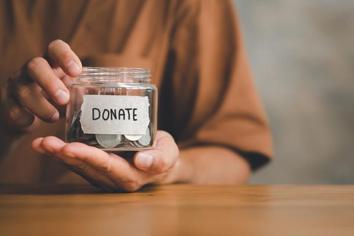 A close up of hands holding a jar with 'donate' written on with coins in the jar