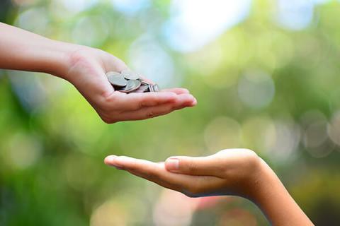 A hand holding coins in reaching out to an empty hand