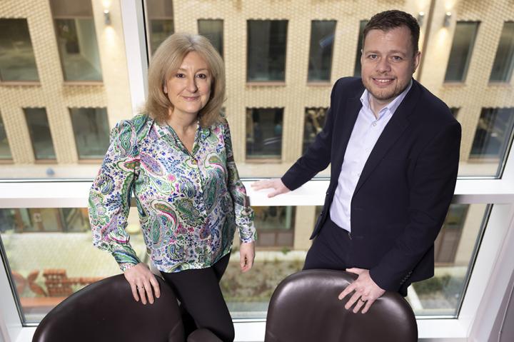 Susan Howe and Colin Churchward standing behind chairs and smiling at the camera