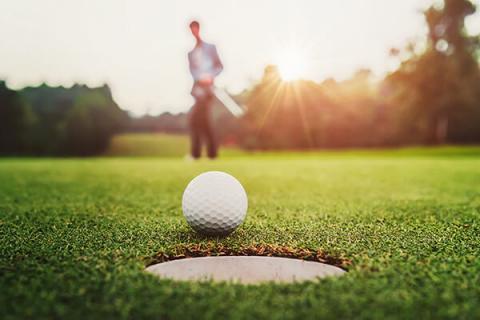 Close up of a golf ball about to go in the hole with a golf player in the background