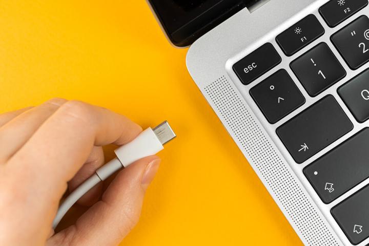 close up of Laptop against a yellow background with hand plugging in charger