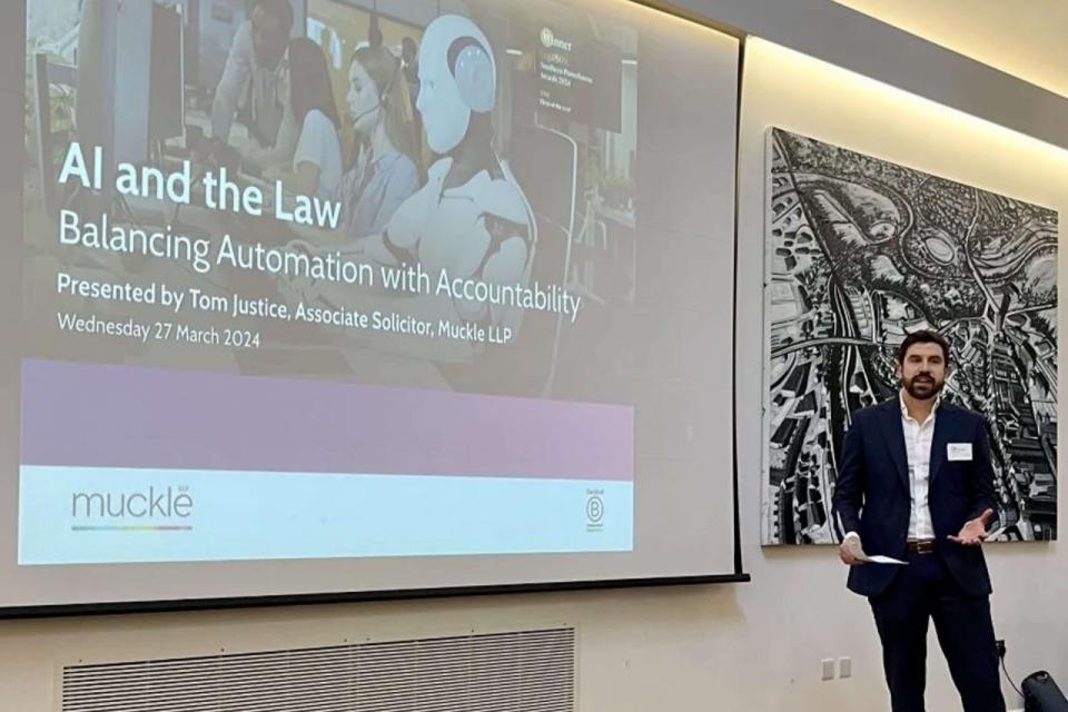 Tom justice, lawyer at Muckle LLP standing in front of a large projector screen with a presentation on it saying AI and the Law