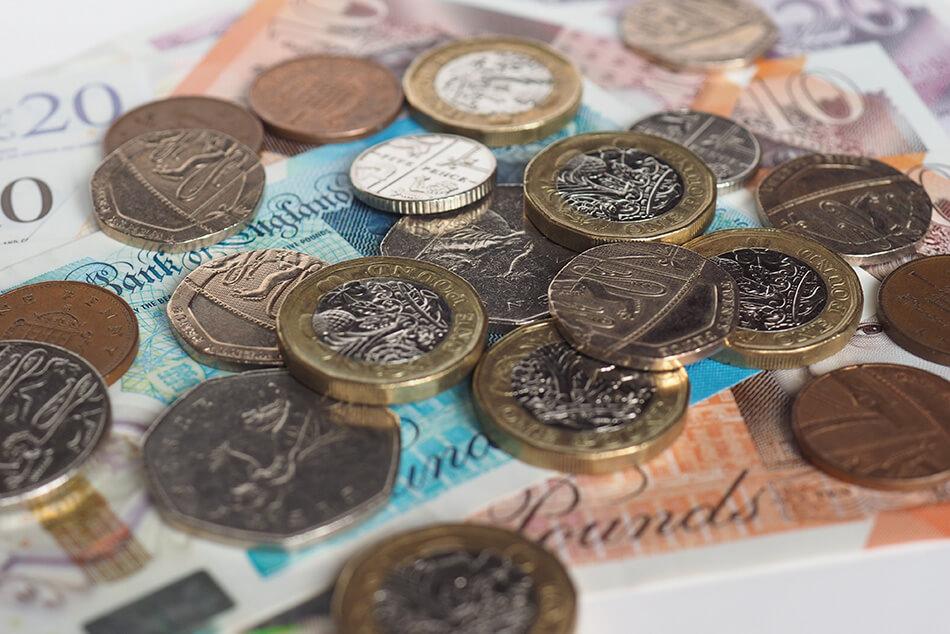 Close up of a mixture of coins on top of a £5, £10 and £20 note