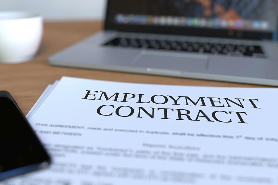 Close up of an employment contract, with a laptop and coffee cup in the background