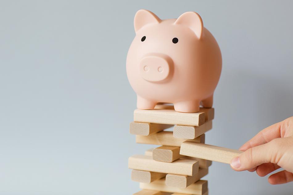 A pink piggypink on top of a Jenga tower, with a hand pulling out a block from the tower