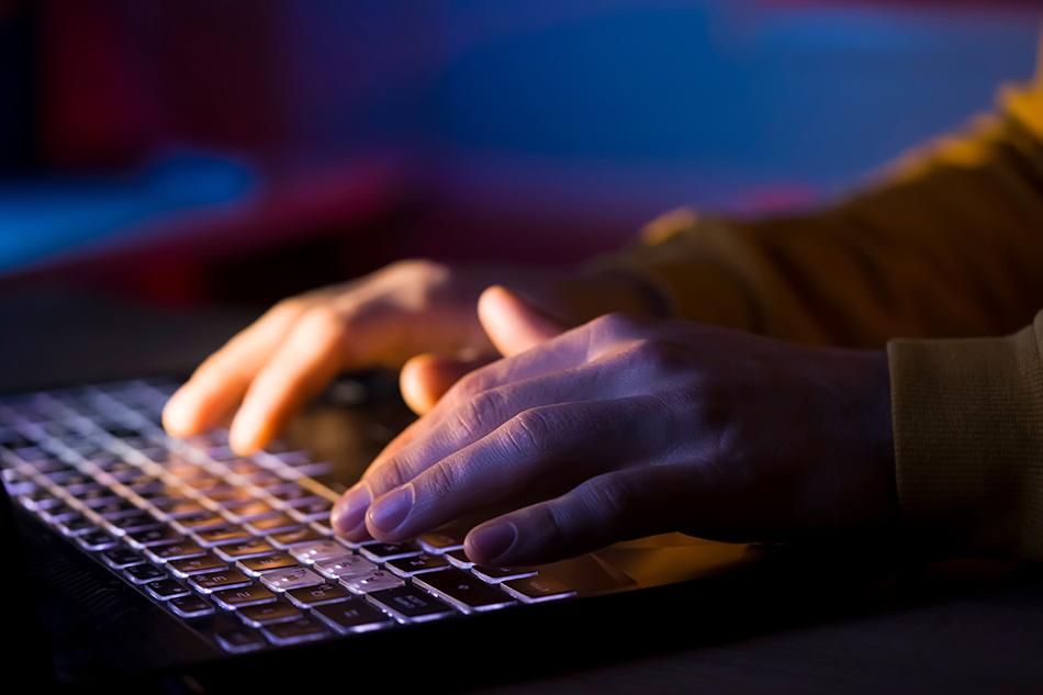Close up of hands typing on a computer keyboard with a dark blue background
