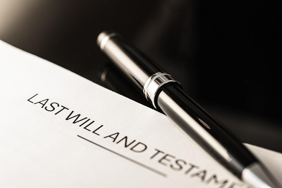 Zoomed in photo of a black pen on cream paper. The top of the paper reads 'Last Will and Testament'.
