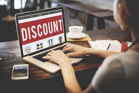 Woman typing on a laptop, the laptop has the word discount written on it in white writing against a red background