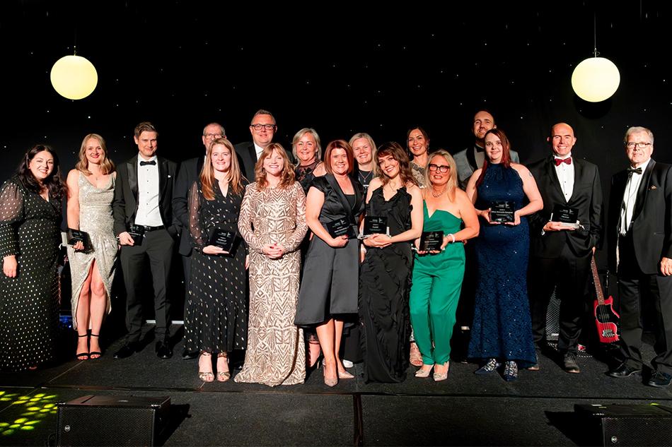 A group of people smartly dressed holding awards and standing on the stage of an awards ceremony