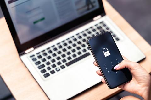 a hand holding a mobile phone with a picture of a padlock on it, in the background is a silver laptop