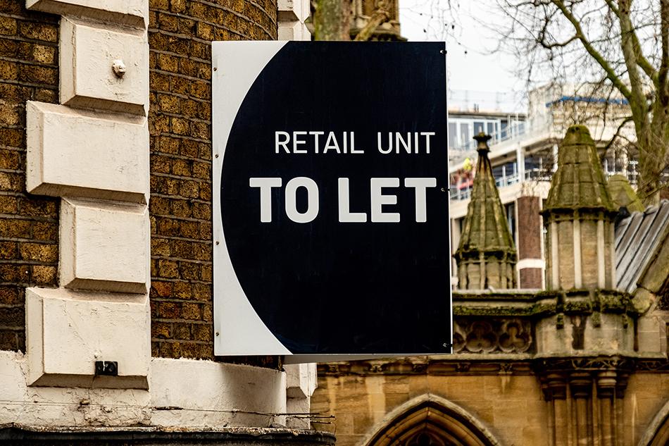 A black and white sign displaying - Retail Unit To Let - on the side of a brown building