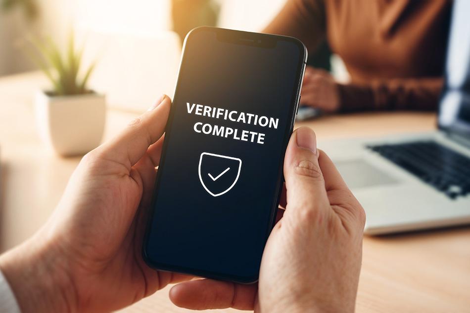 Picture of a hand holding a phone with verification complete and a tick written on it