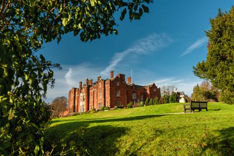 A country estate house sitting on top of a hill, there are trees in the foreground of the picture