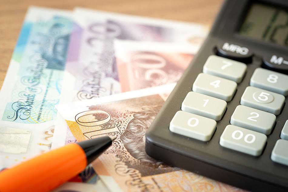 Close up of a black calculator and orange pen on top of a £10, £50, £20 and £5 note