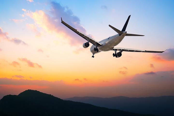 A plane flying over a sunset and mountains