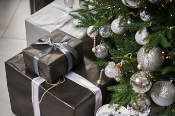 Presents wrapped in black and silver paper under a Christmas tree with silver baubles