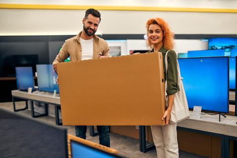 A man and woman carrying a brand new TV through an electronic store