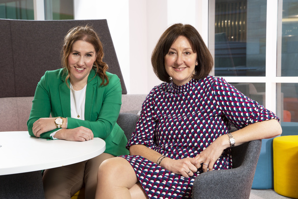 Gillian Scribbins (left) and Susan Howe sit in a modern office and smile at the camera.